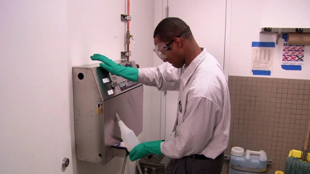 Janitorial service San Jose CA technician sanitizing wall-mounted dispenser with goggles